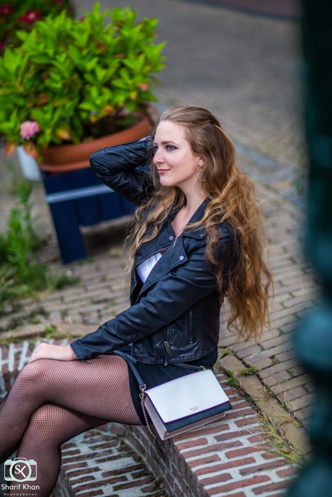 Female model Marina Krivonossova runs her hand through her hair during a fashion photoshoot on the streets of a city in the Netherlands. Marina smiles into the distance.