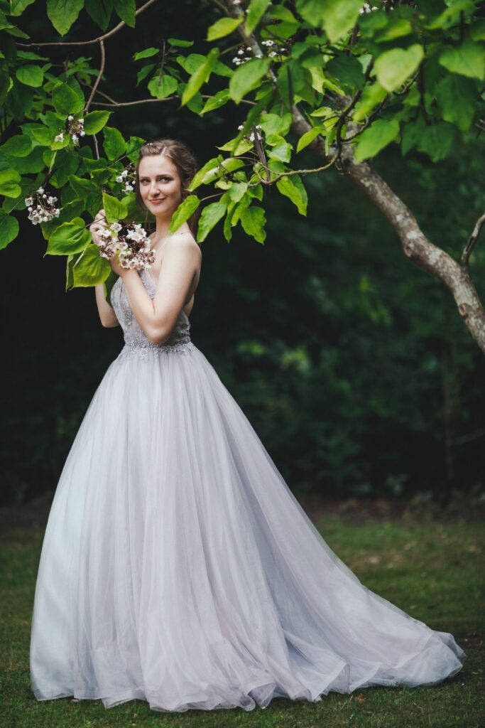 Female model Marina Krivonossova holds a tree branch with flowers as she smiles and looks into the distance. Marina is posing for a wedding photoshoot in Denmark in nature.
