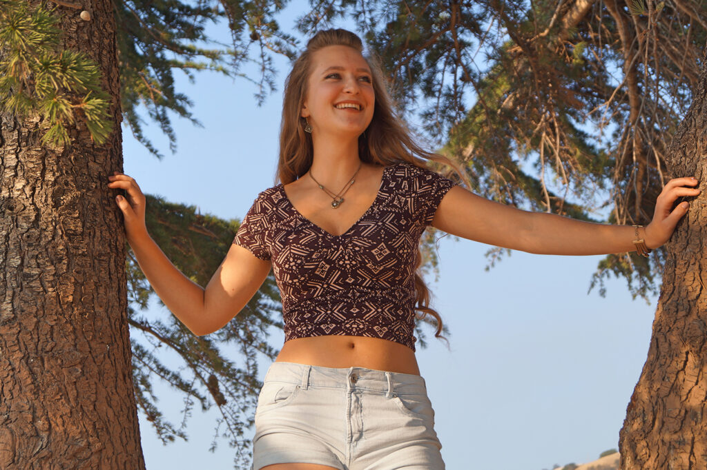 Female model Marina Krivonossova looks into the distance and smiles. Marina has climbed a tree during a nature photoshoot in California.