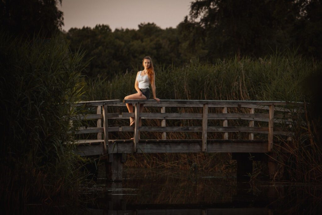 Female model Marina Krivonossova sits on a bridge surrounded by nature. Marina looks longingly into the distance.