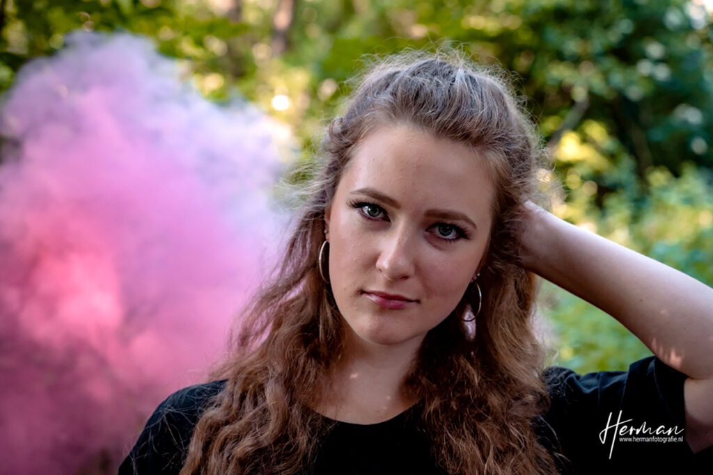 Female model Marina Krivonossova looks into the camera during a smoke bomb photoshoot taking place in a nature park.