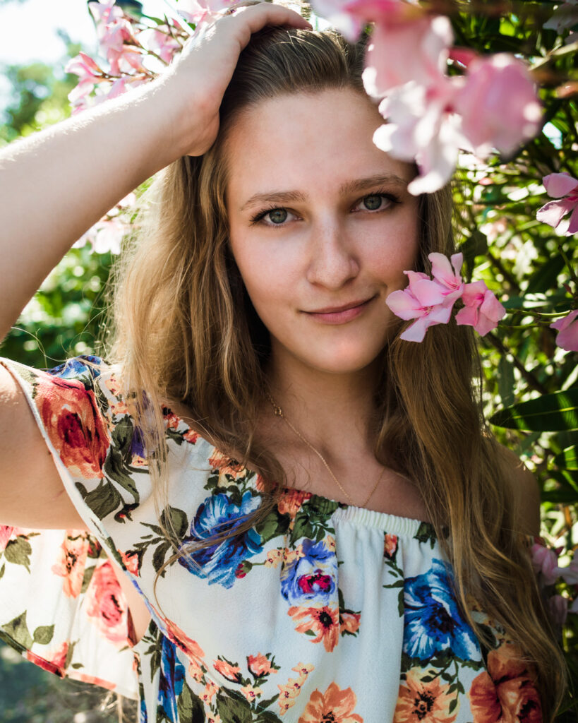 Female model Marina Krivonossova runs a hand through her hair during a nature photoshoot with flowers.