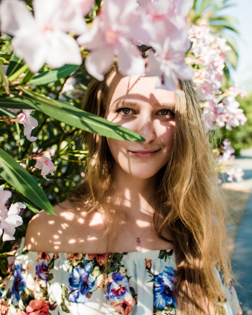 Female model Marina Krivonossova smiles at the camera as she shadows of branches and flowers fall on her during a photoshoot in California.
