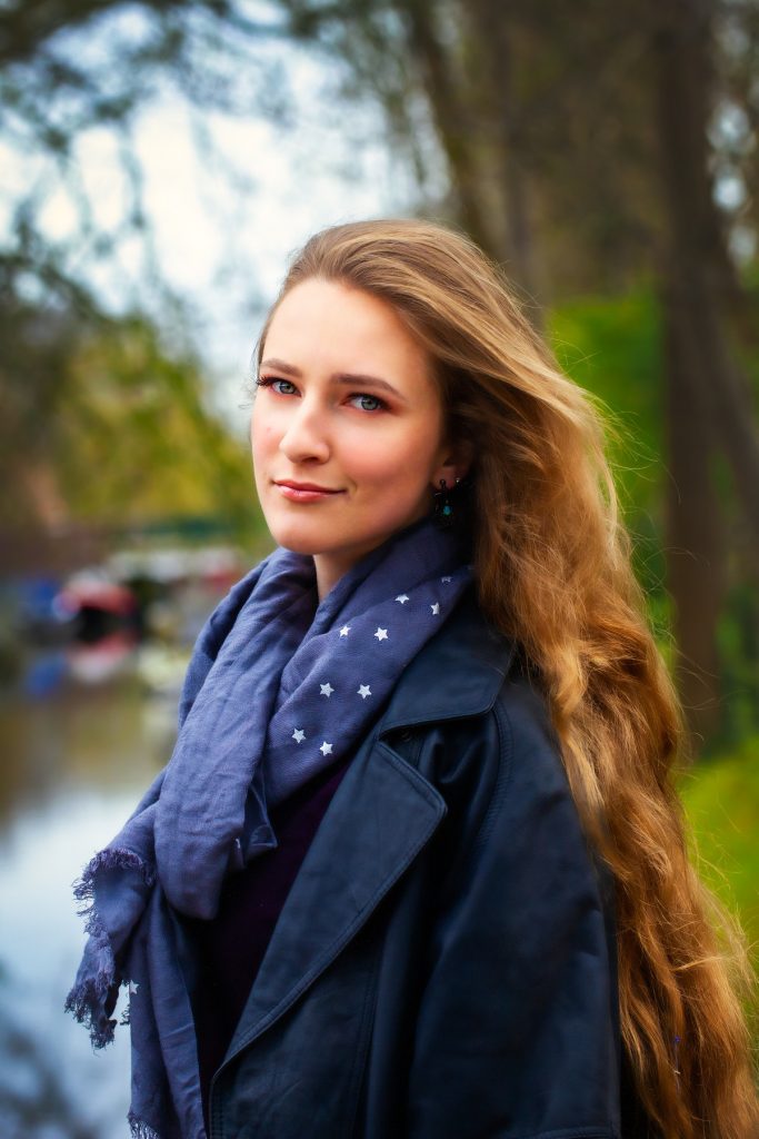 Female model photoshoot image. She smiles at the camera during a fashion photoshoot near a canal in a city in the Netherlands.