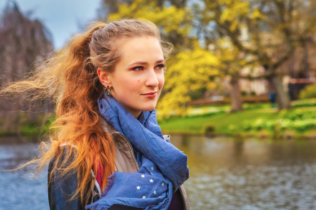 Female model photoshoot image. She looks into the distance during a fashion photoshoot taking place in a city in the Netherlands. Canal and beautiful nature in the background.